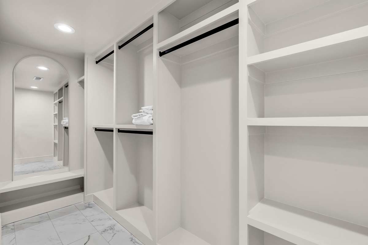 A spacious walk-in closet featuring elegant white cabinets and stylish mirrors, enhancing the sense of openness and organization.