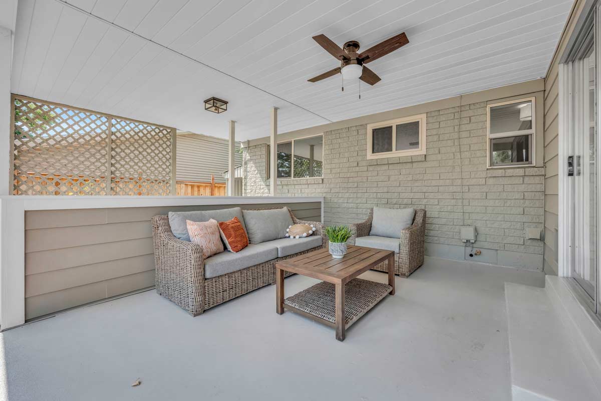 A cozy patio featuring a comfortable couch, a stylish table, and a ceiling fan for a refreshing breeze.