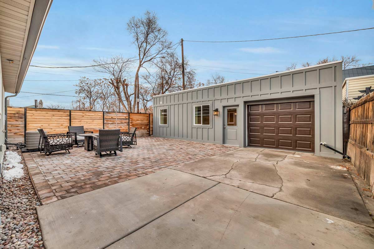 A backyard featuring a spacious patio and a garage, surrounded by greenery and outdoor elements.