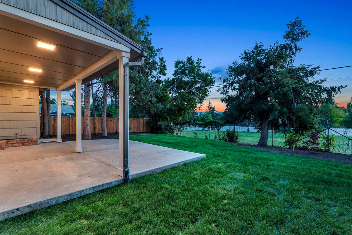 A serene backyard featuring a covered patio surrounded by lush green grass, perfect for relaxation and outdoor gatherings.