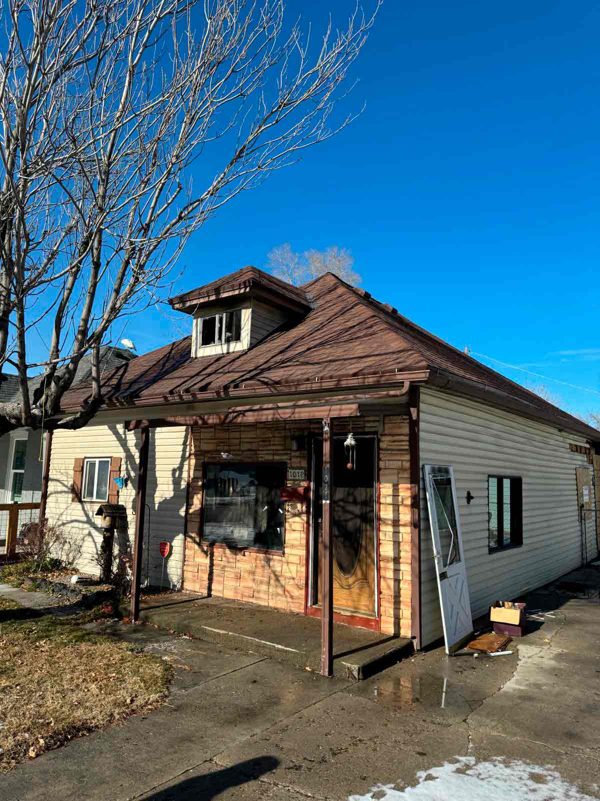 A small house with a brown roof and a car parked in front, set against a clear sky.